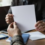 Dirigeant de TPE vérifiant une fiche de paie vierge à côté d'un ordinateur portable fermé