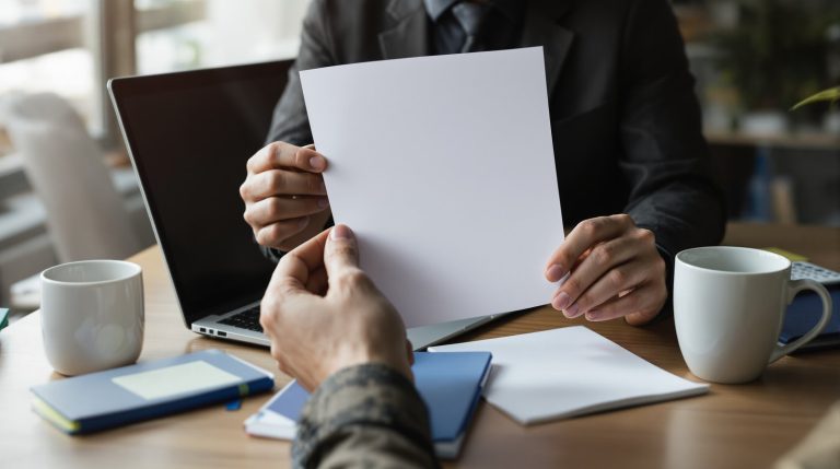 Dirigeant de TPE vérifiant une fiche de paie vierge à côté d'un ordinateur portable fermé