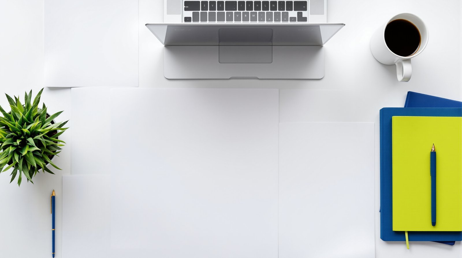 Bureau vu du dessus avec des feuilles blanches vierges disposées en grille façon tableau comparatif, ordinateur portable, carnets indigo et vert citron — comparatif logiciels RH 2026 LogicielRH